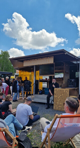 foto von der offenen b&uuml;hne vom energiemobilh&uuml;tte, das publikum sitzt auf gras und in orangefarbenen liegest&uuml;hlen