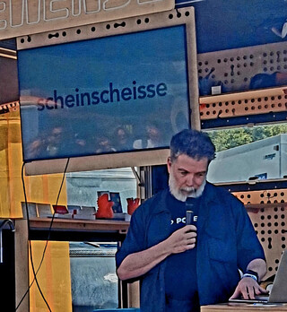 auf dem monitor steht: &bdquo;scheinscheisse&ldquo;, ich spreche in ein mikorofon