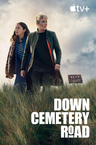 filmplakat f&uuml;r die serie &bdquo;down cemetery road&ldquo; auf apple tv. zwei frauen stehen auf einer grasbewachsenen anh&ouml;he mit einem verwitterten schild im hintergrund. sie blicken in die ferne, gekleidet in l&auml;ssige jacken vor einem bew&ouml;lkten himmel.