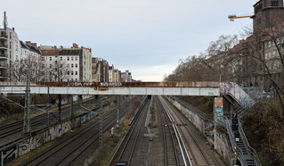 foto von von einer fussg&ouml;ngerbr&uuml;cke &uuml;ber die bahngleise zwischen gesundbrunnen und sch&ouml;nahuser allee. alles sieht grau-braun aus, ausser ein paar weiss-verwaschender mehrfamilienh&ouml;user links.