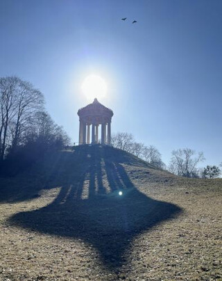 Im Gegenlicht auf einer Anh&ouml;he ein Tempelchen, das einen riesigen Schatten auf den wintergrasigen Hang davor wirft